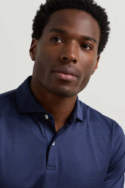 A close-up shot of a man wearing a navy blue long-sleeve polo shirt with a subtle textured pattern, set against a plain light gray background.