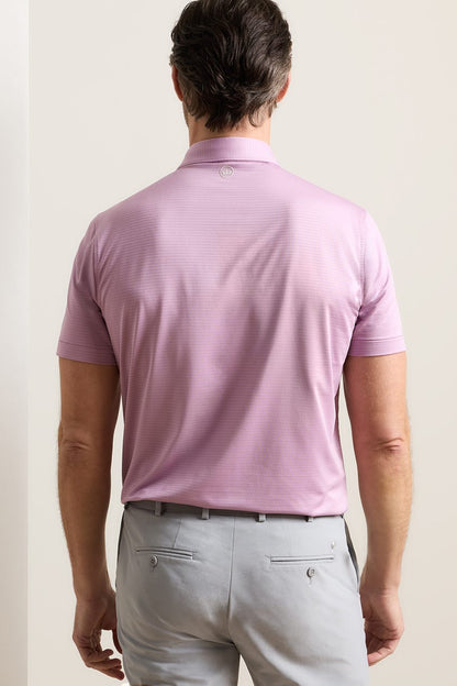 A man viewed from behind wearing a light pink short-sleeve polo shirt and light gray trousers, standing against a plain off-white background.