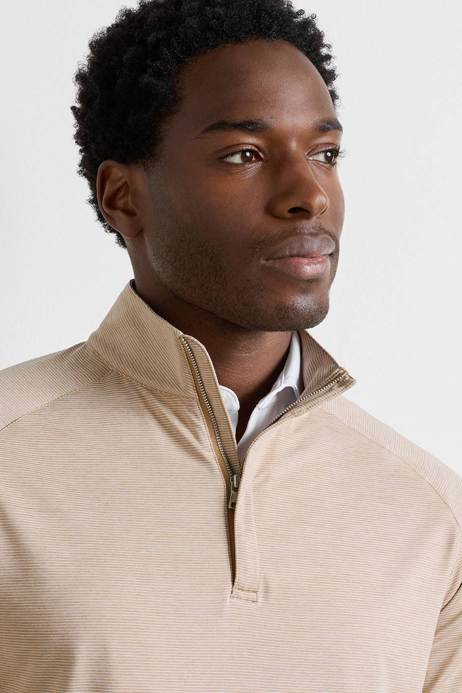 A man wearing a beige quarter-zip pullover sweater over a white collared shirt, shown in a close-up profile against a light gray studio background.
