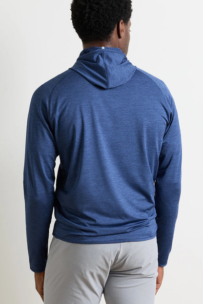A man viewed from behind wearing a heathered blue long-sleeve athletic hoodie and light gray pants, standing against a plain off-white wall.