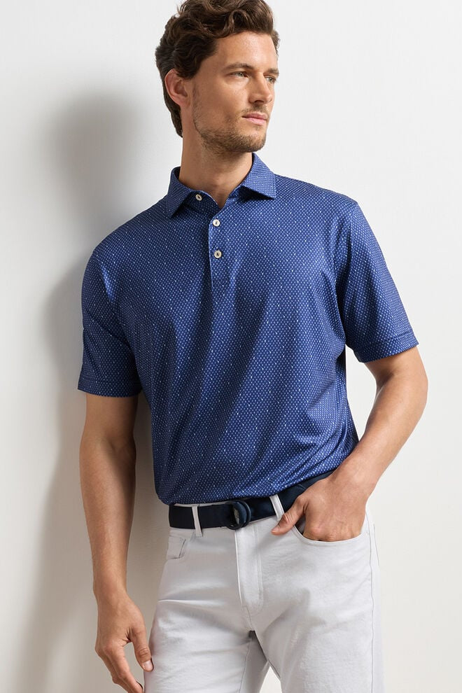 Man wearing a blue patterned polo shirt and white pants against a light background