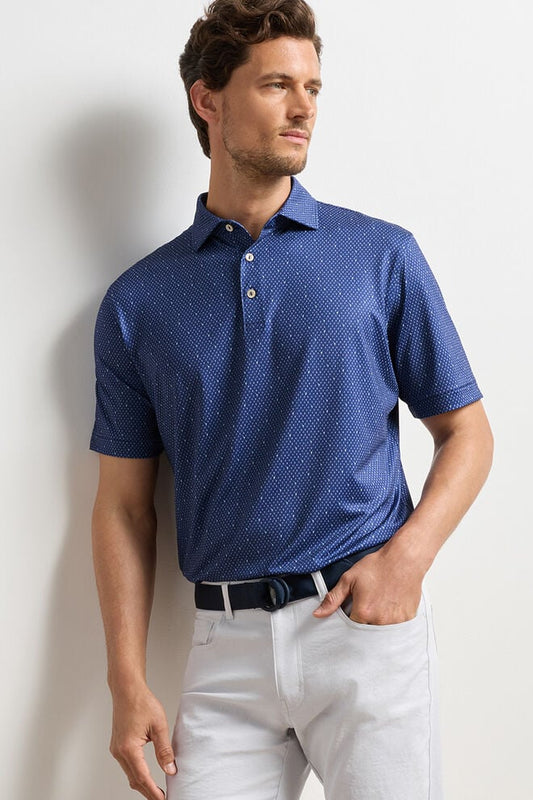 Man wearing a blue patterned polo shirt and white pants against a light background
