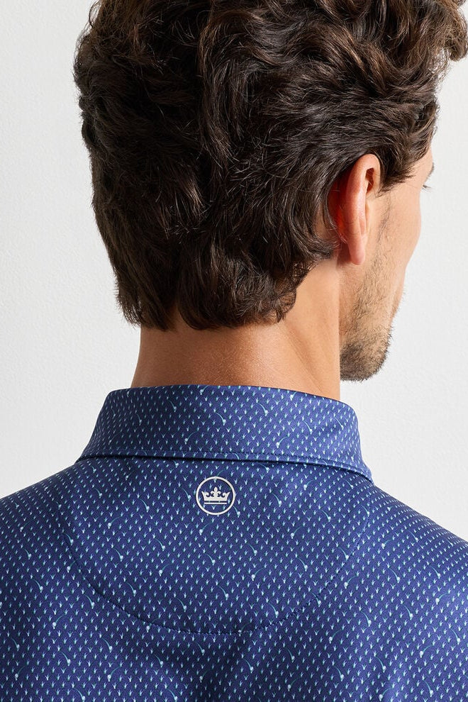 Man wearing a blue patterned shirt with a visible brand logo on a light gray background