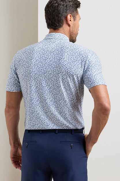 Man wearing a blue patterned shirt and navy pants against a plain background