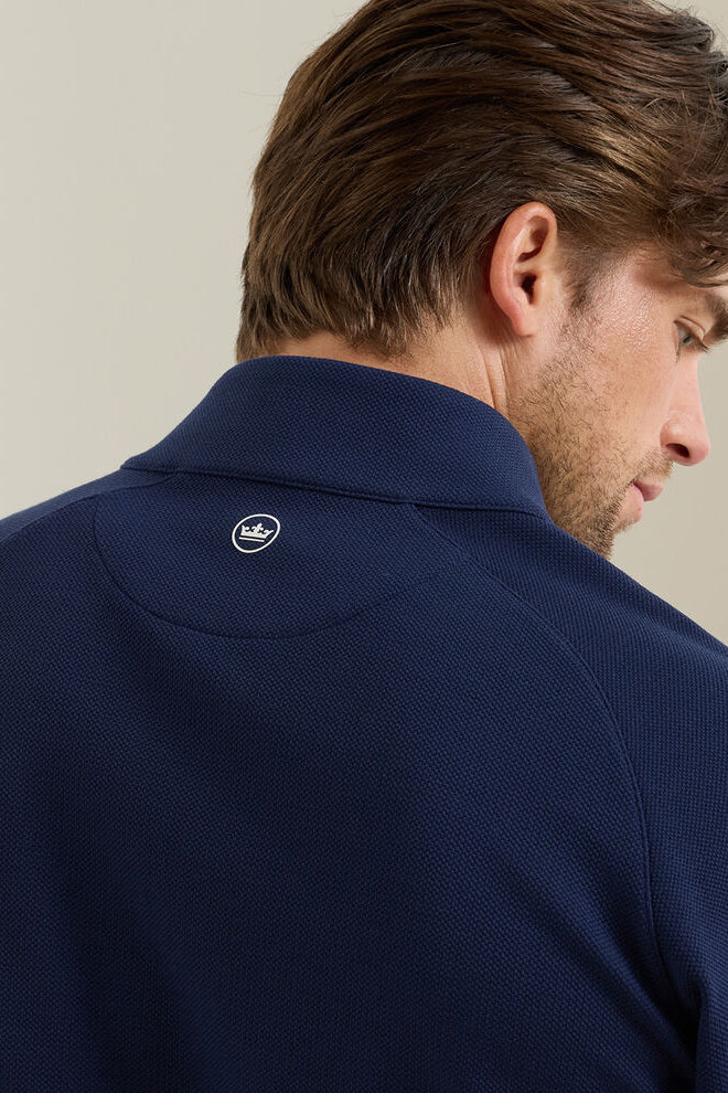 Man wearing a navy blue polo shirt with a brand logo on the collar against a neutral background