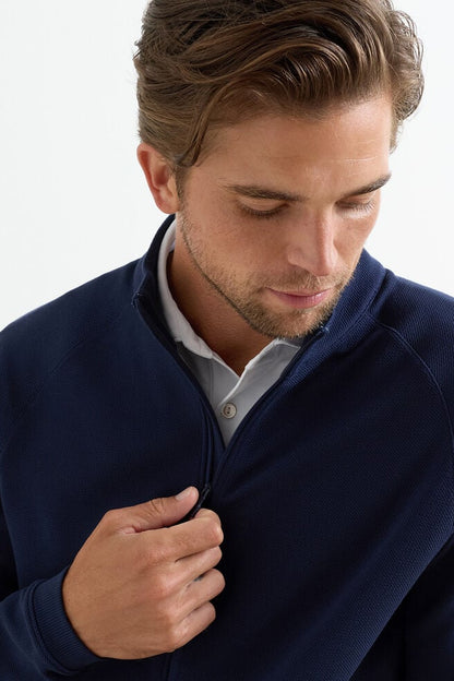 Man wearing a navy blue sweater over a white shirt on a light gray background