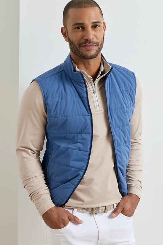Man wearing a blue puffer vest over a beige shirt on a light gray background
