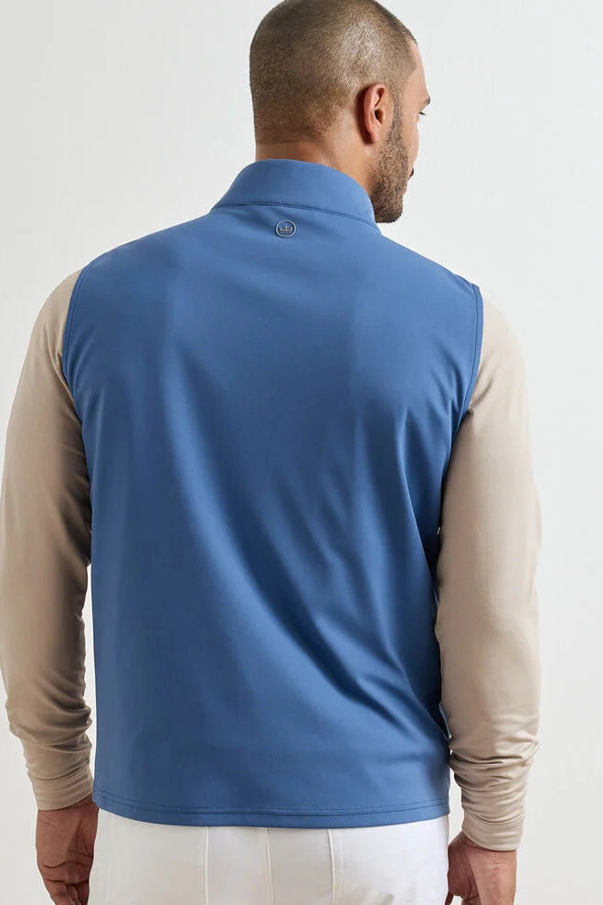 Man wearing a blue vest over a beige long-sleeve shirt on a white background