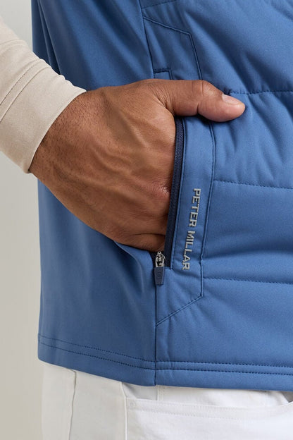 Blue jacket with a hand reaching into a pocket, brand 'Peter Millar' visible.
