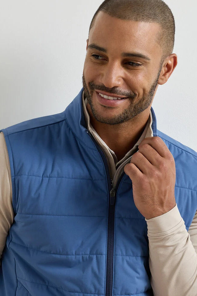 Man wearing a blue puffer vest against a plain background