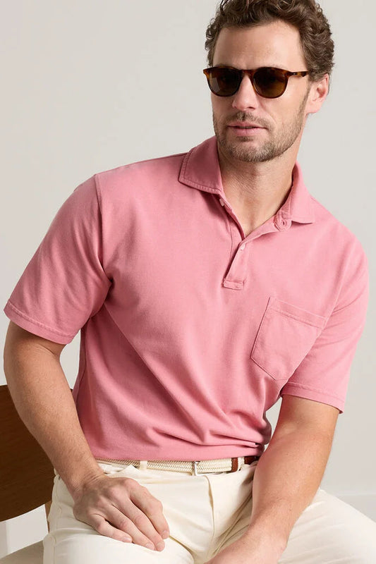Man wearing a pink polo shirt and sunglasses sitting against a plain background