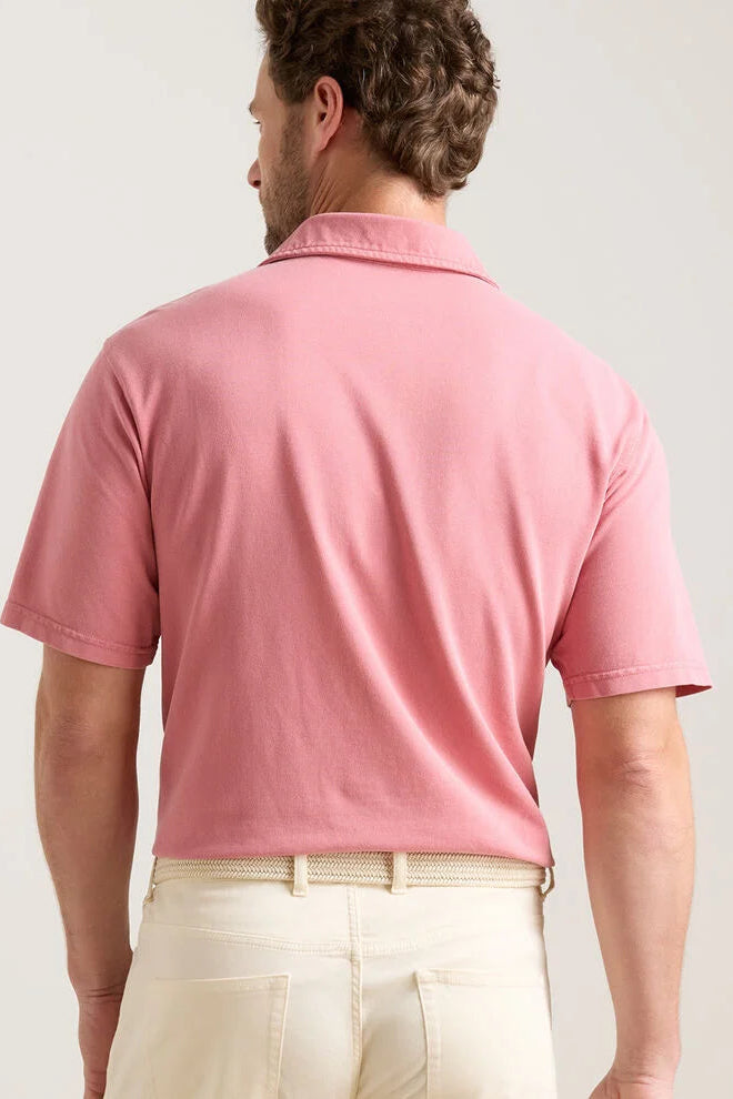 Man wearing a pink polo shirt and beige pants on a plain background