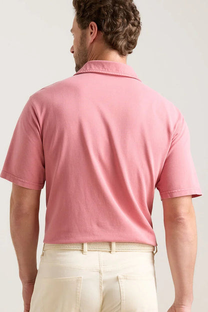 Man wearing a pink polo shirt and beige pants on a plain background