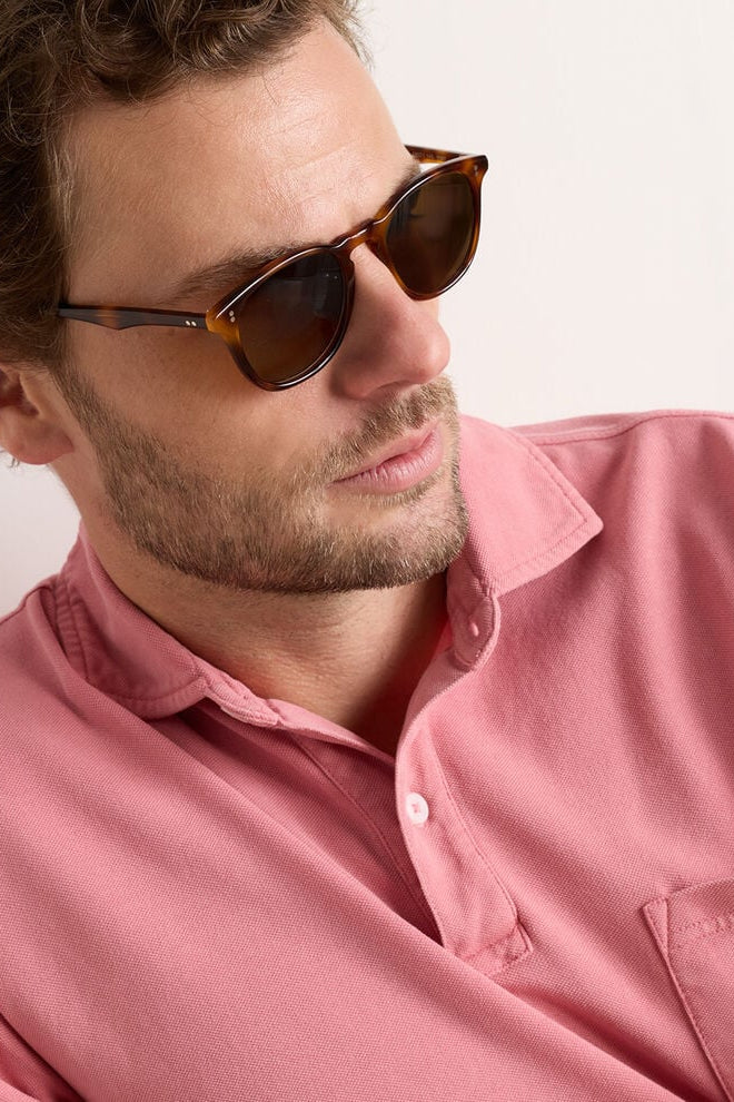 Man wearing sunglasses and a pink shirt against a white background
