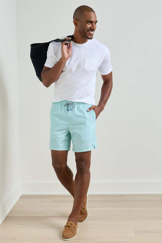 Man wearing a white t-shirt and light blue shorts, holding a black bag, against a plain background.