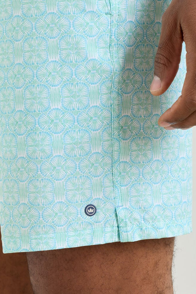 Close-up of a person wearing light blue patterned shorts with a brand logo on a neutral background