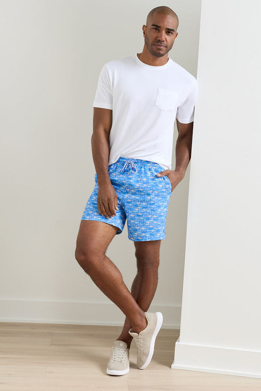 Man wearing a white t-shirt and blue patterned shorts against a plain background