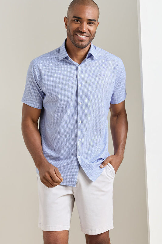 Man wearing a light blue short-sleeve shirt and white shorts against a plain background