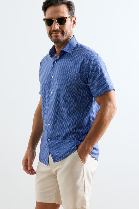 Man wearing a blue patterned shirt and beige shorts on a white background