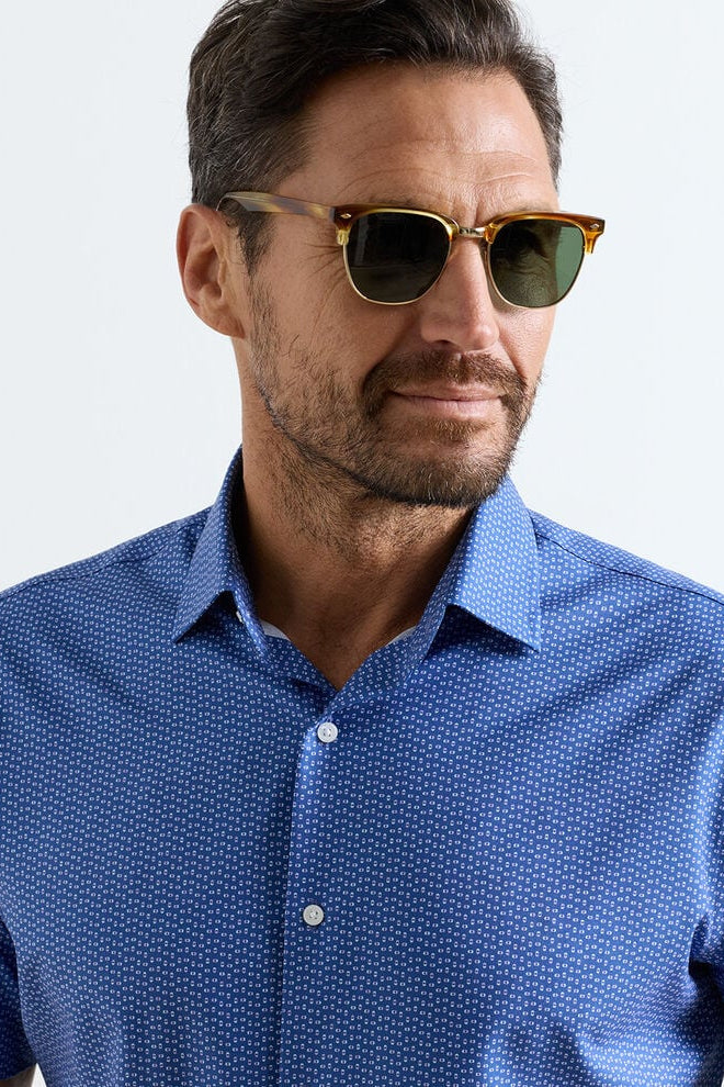 Man wearing a blue patterned shirt and sunglasses against a light gray background