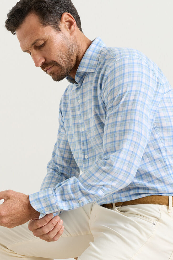 Man wearing a blue plaid shirt and beige pants against a white background