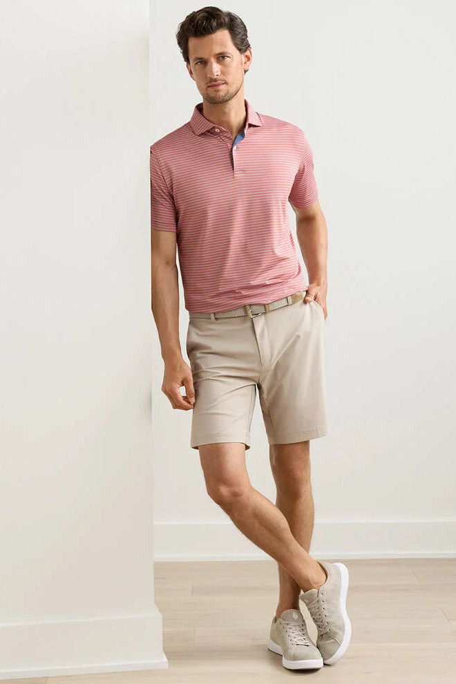 Man wearing a pink striped polo shirt and beige shorts against a white wall.