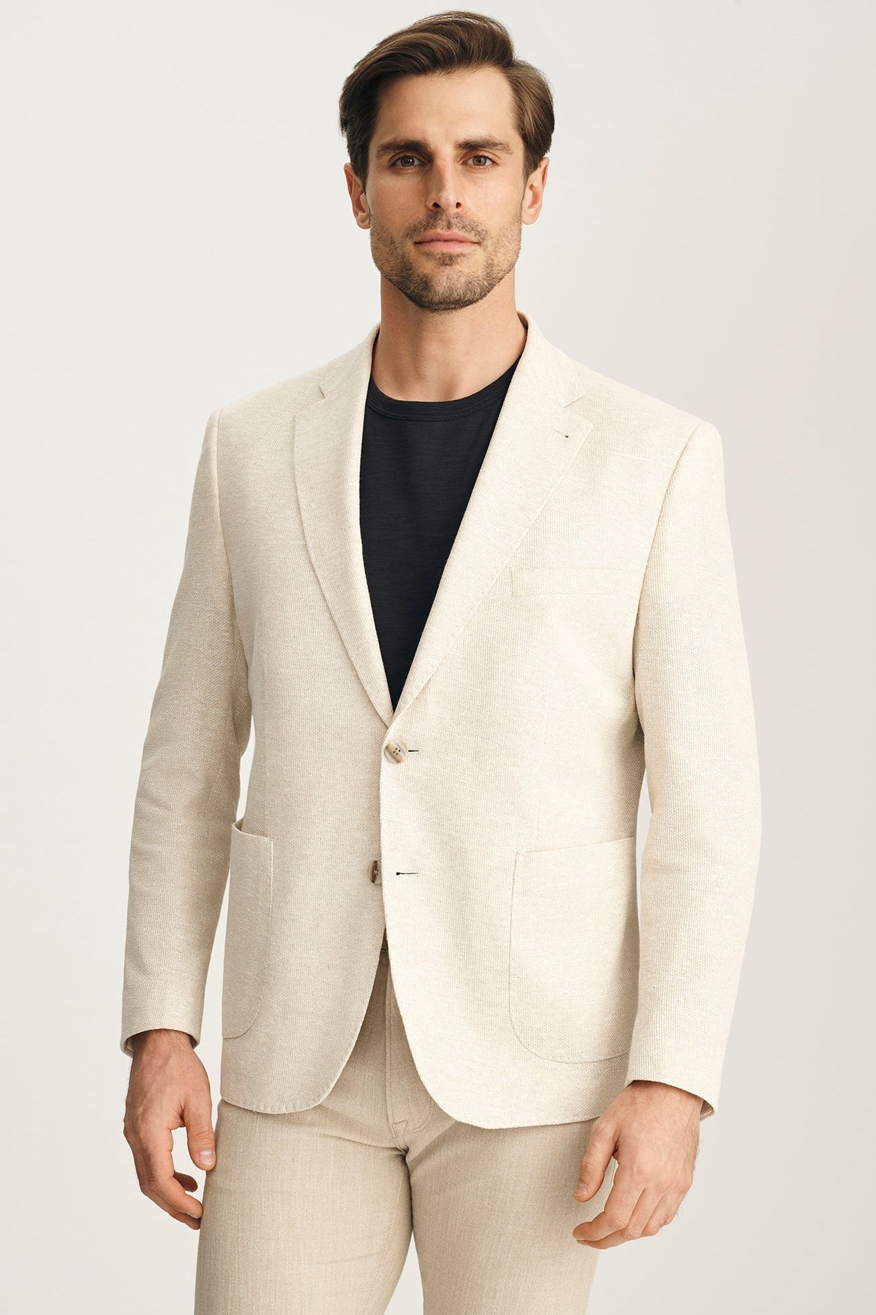 Man wearing a light beige suit with a black shirt on a white background