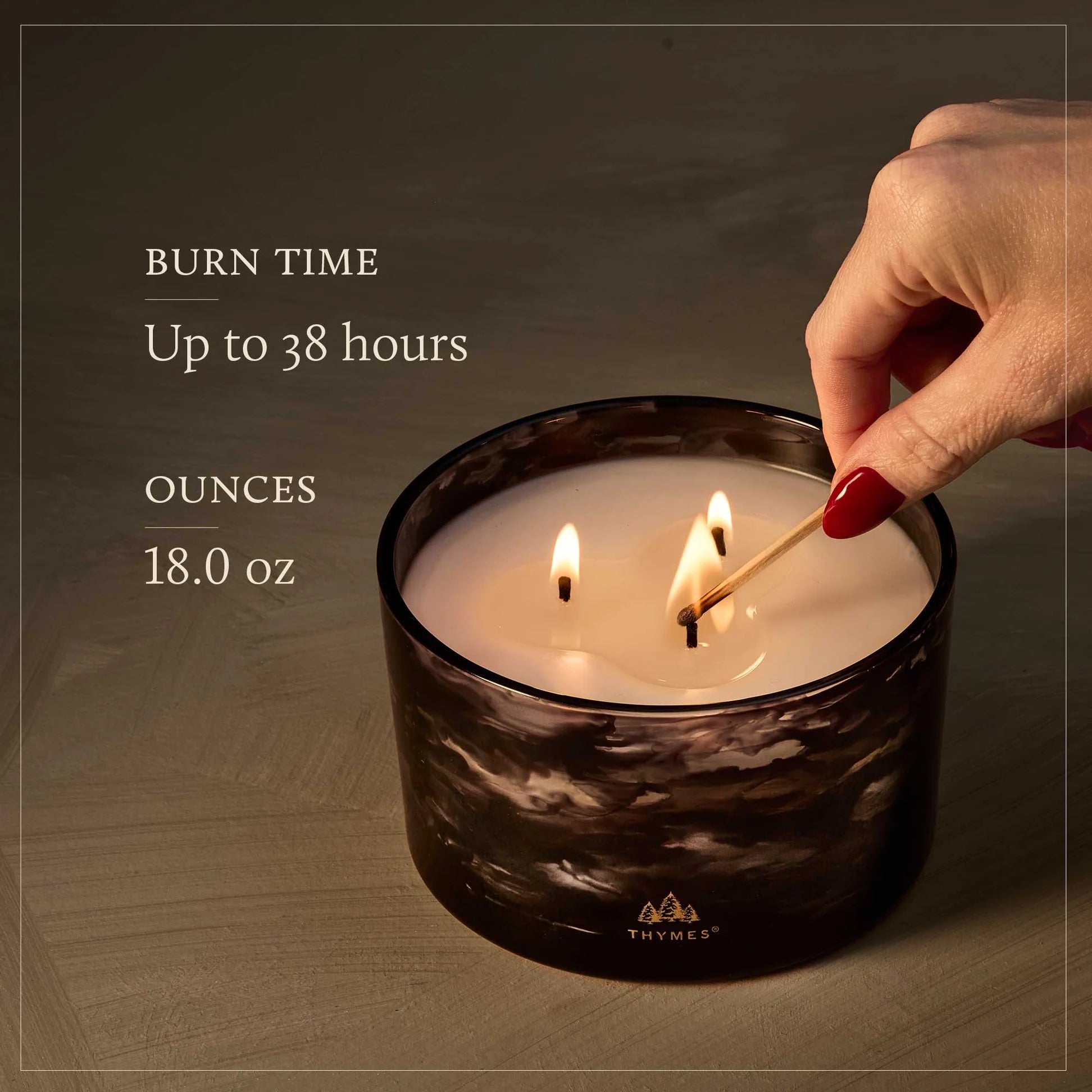 Candle being lit with a match, Thymes logo visible, on a wooden surface.
