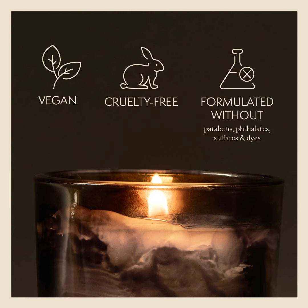 Candle in a glass holder with vegan, cruelty-free, and sulfate-free icons on a dark background.