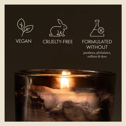 Candle in a glass holder with vegan, cruelty-free, and sulfate-free icons on a dark background.