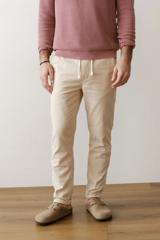 Person wearing a pink sweater and beige pants standing on a wooden floor with a white wall background
