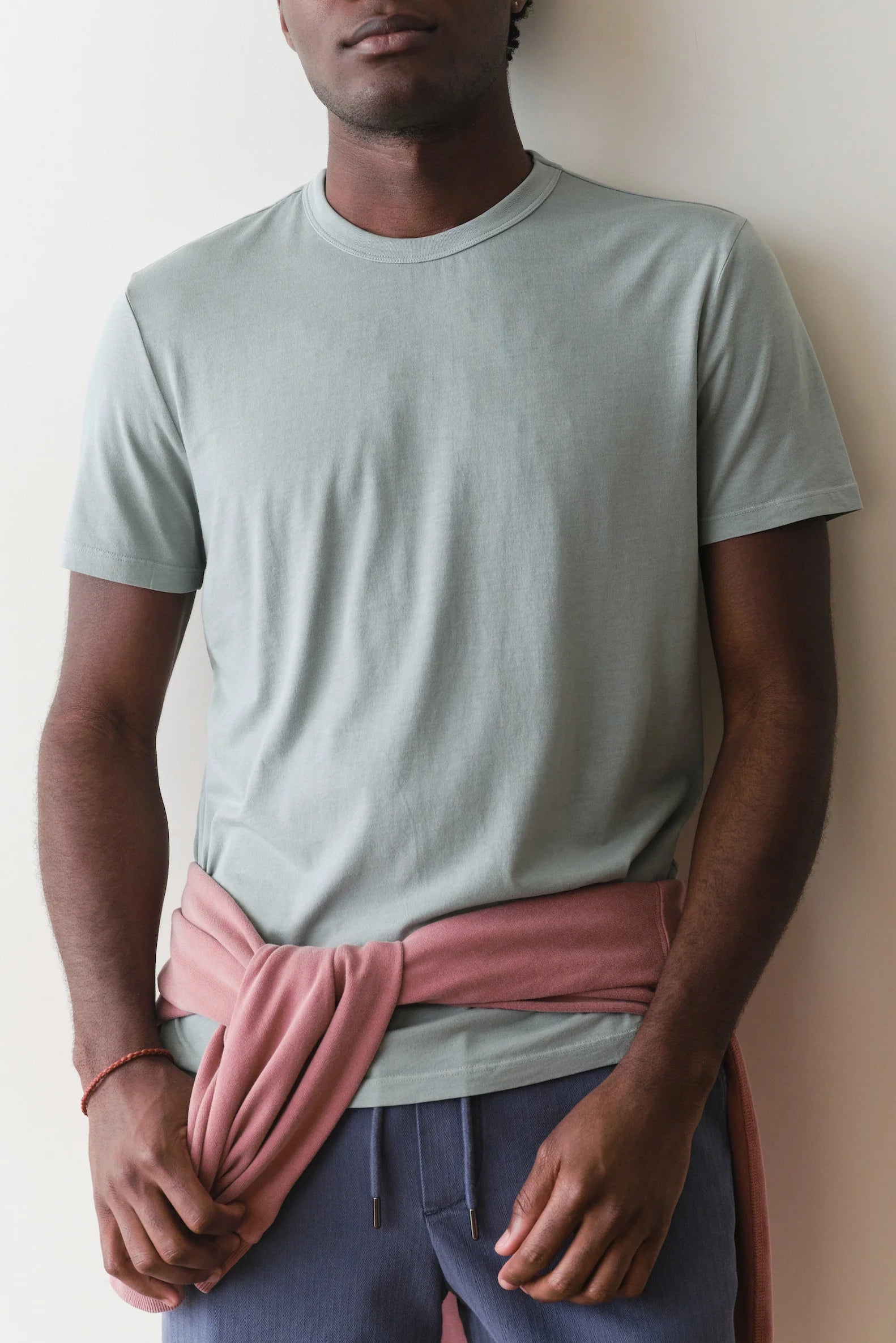 Person wearing a light gray t-shirt and pink fabric around the waist against a plain background