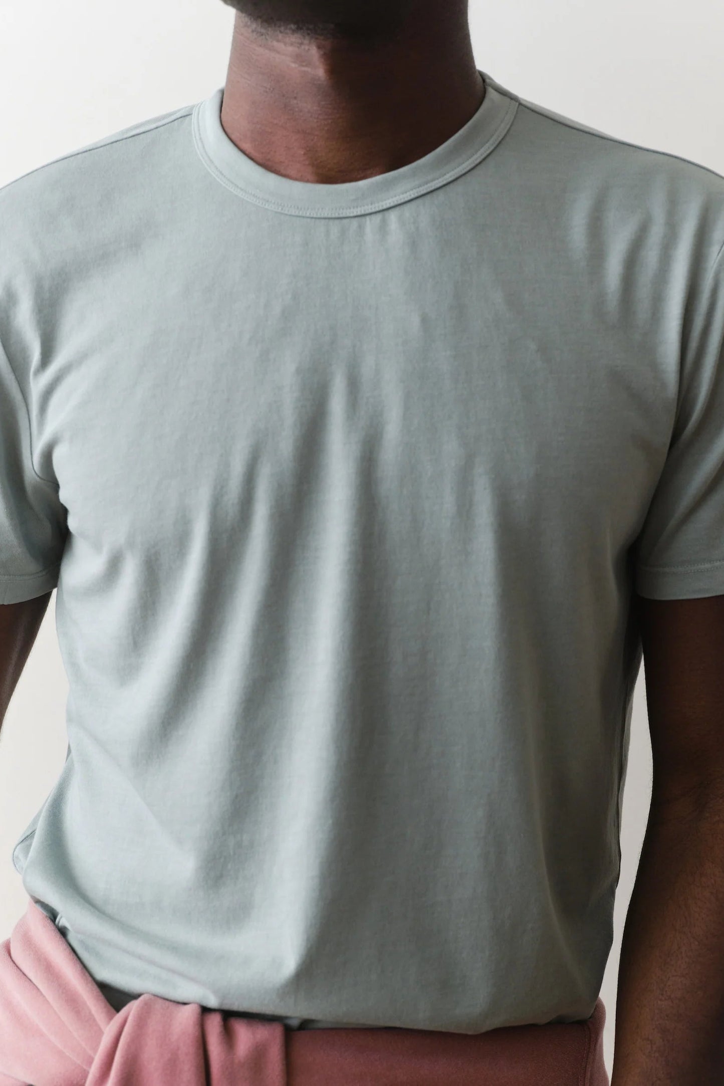 Person wearing a light gray t-shirt and pink pants against a plain background