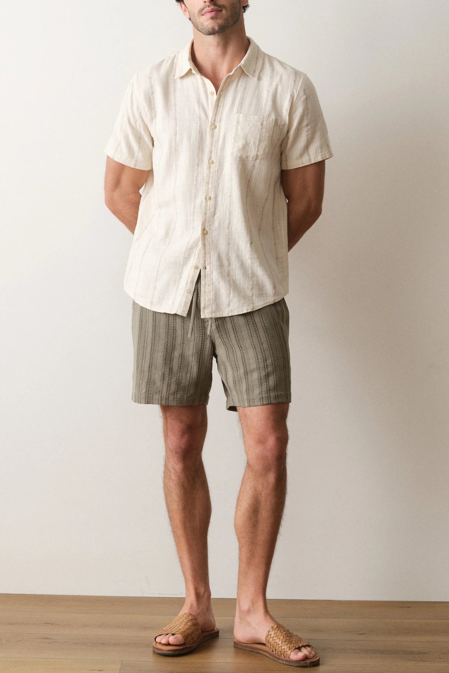 Man wearing a light-colored shirt and striped shorts standing against a plain background