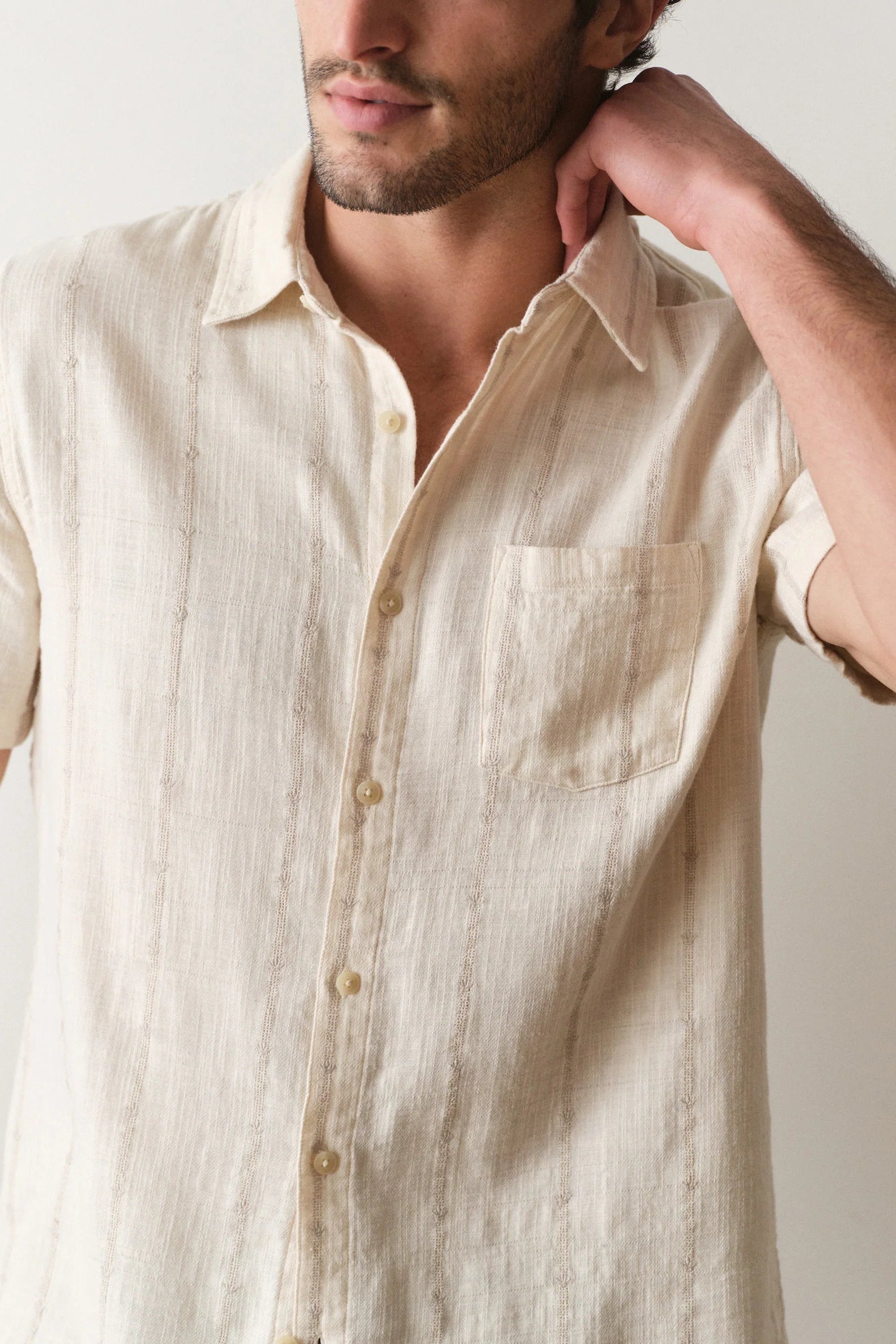 Man wearing a beige short-sleeve shirt against a plain background