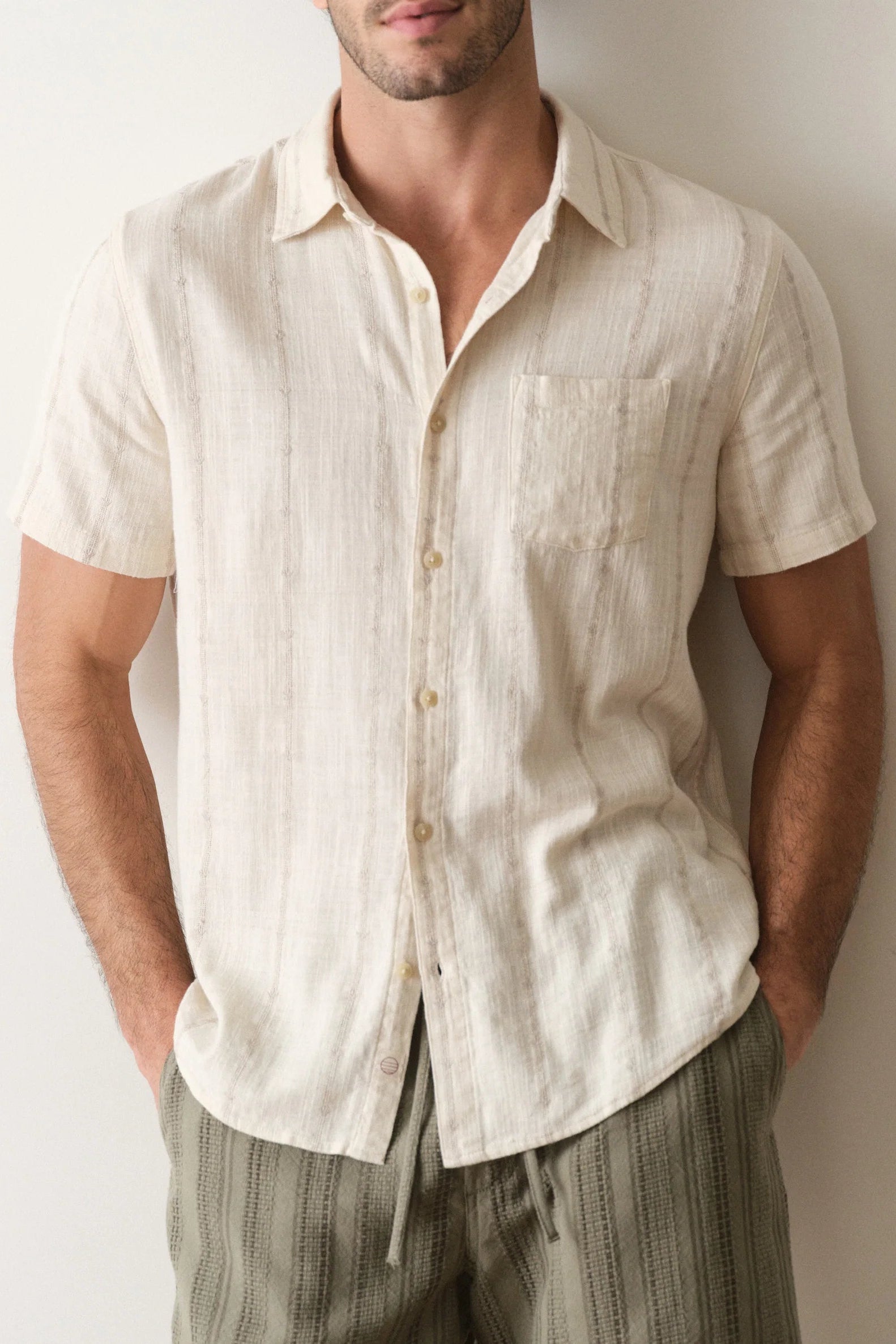 Man wearing a beige short-sleeve shirt against a plain background