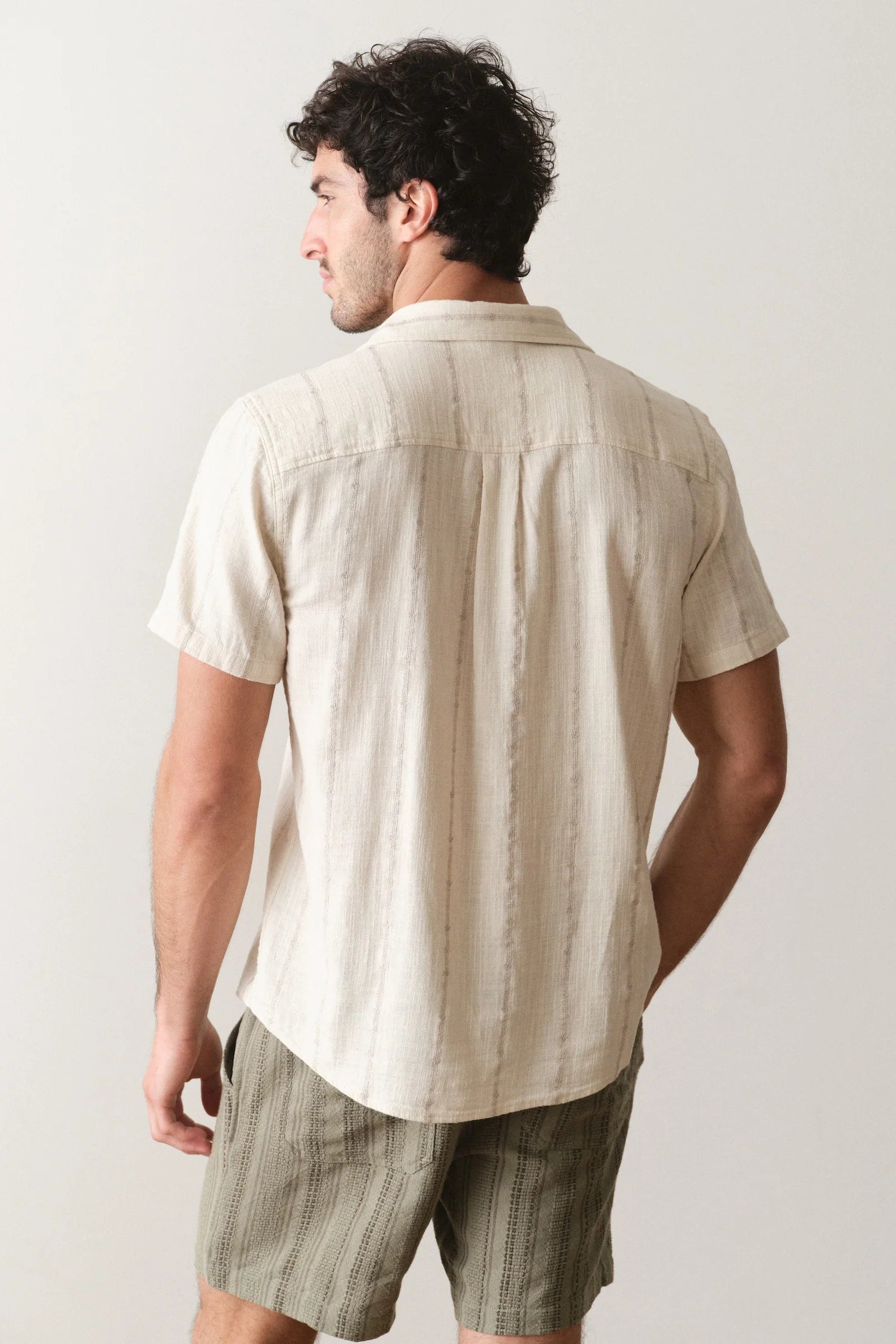Man wearing a beige striped shirt and green shorts against a plain background