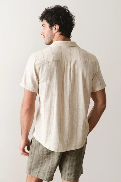 Man wearing a beige striped shirt and green shorts against a plain background