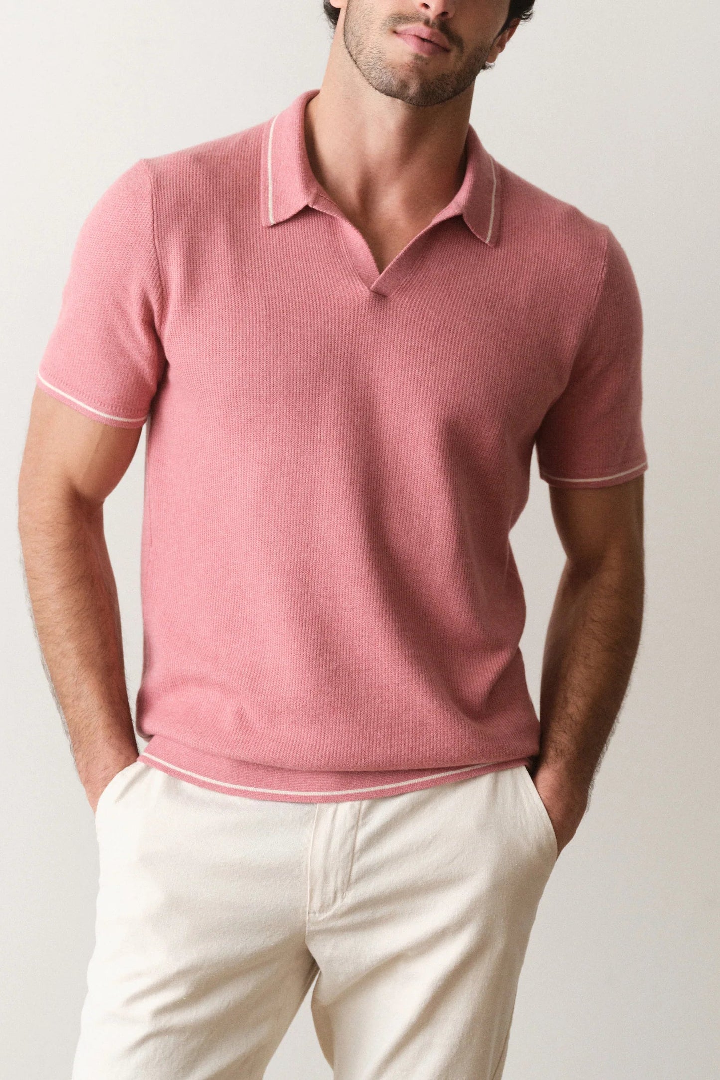 Man wearing a pink ribbed polo shirt and white pants against a plain background