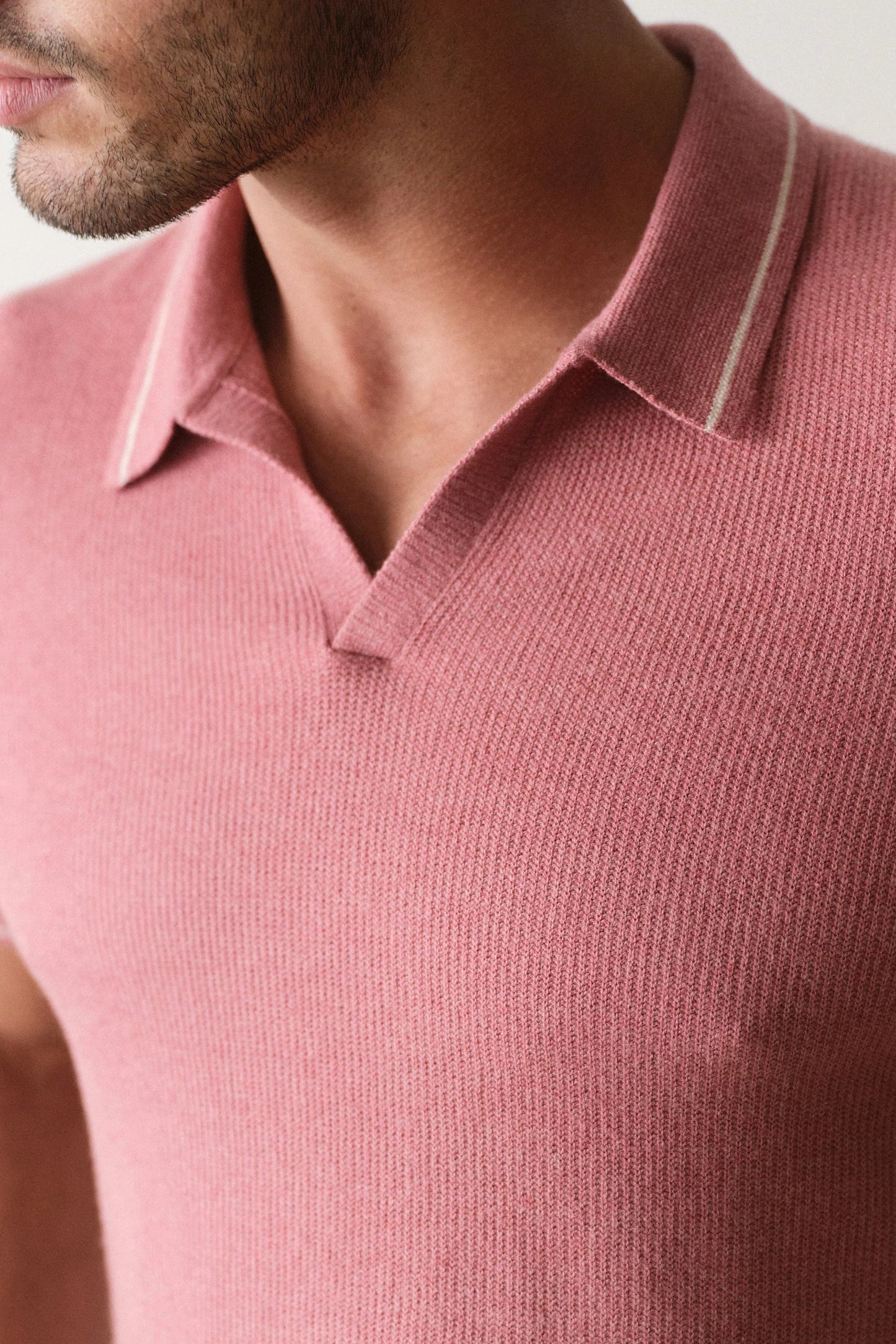 Close-up of a person wearing a pink polo shirt with a neutral background