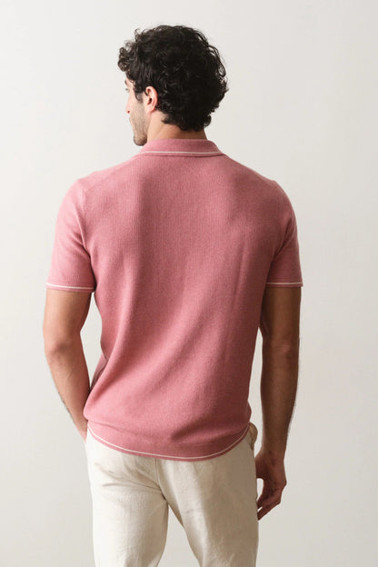 Man wearing a pink polo shirt and light-colored pants against a plain background