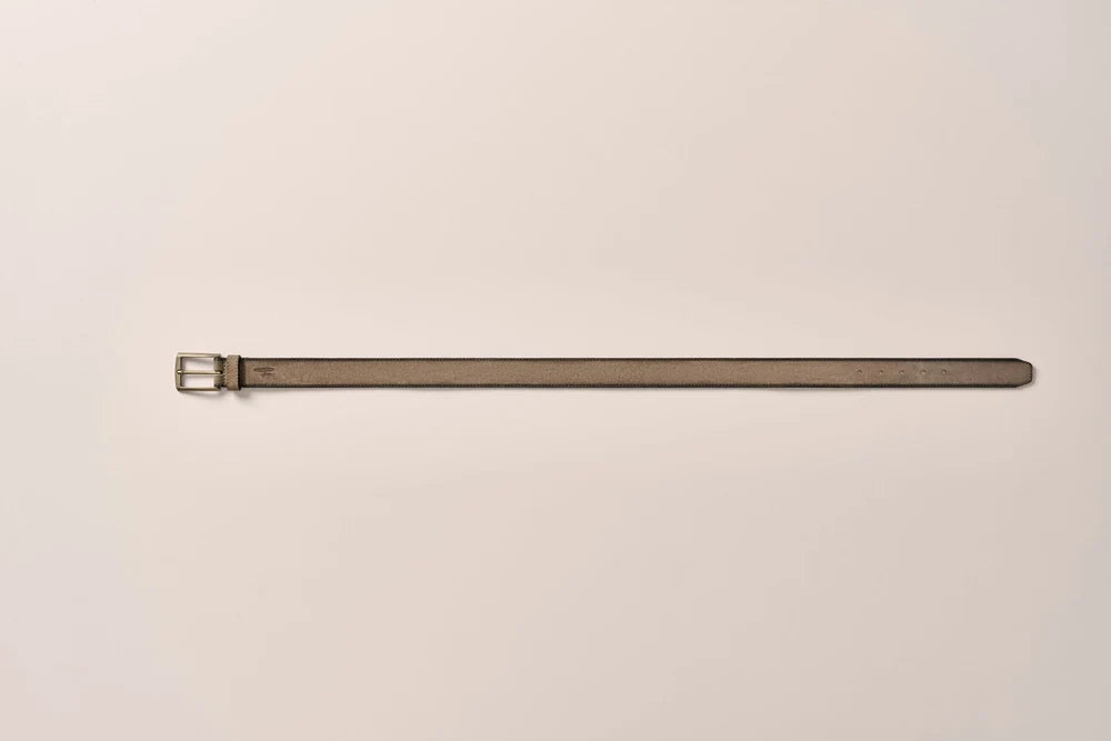 A long, slim leather belt in a muted taupe-brown color with a silver-toned metal buckle, laid horizontally on a plain off-white background.