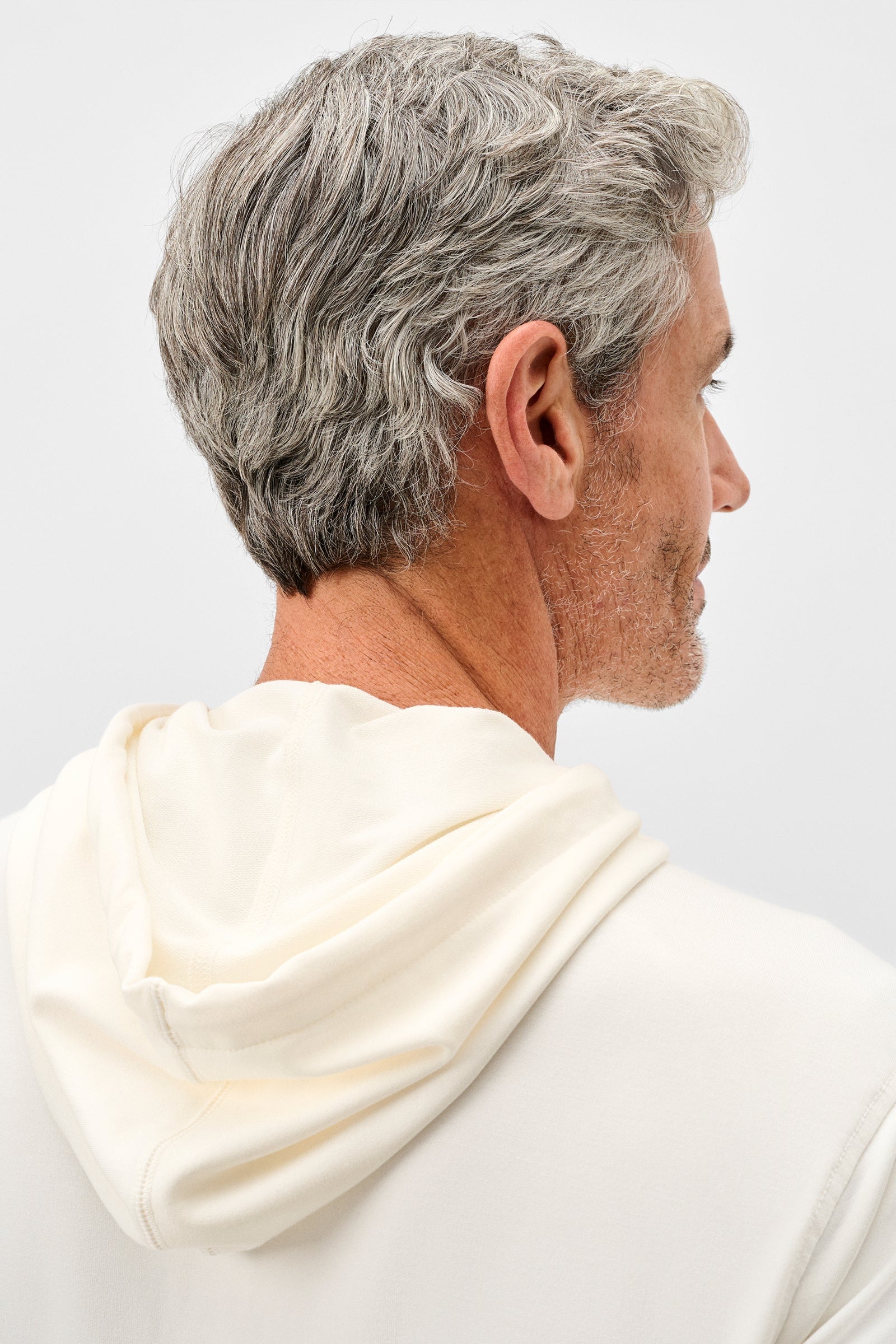 Man wearing a white hoodie with gray hair on a light gray background