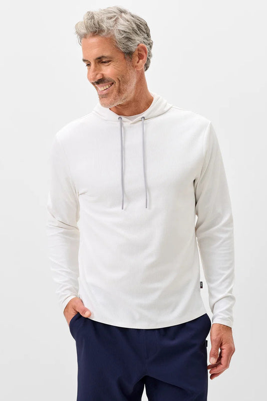 A smiling middle-aged man with gray hair and a beard wearing a white long-sleeve athletic hoodie with gray drawstrings and navy blue pants, standing against a light gray studio background.