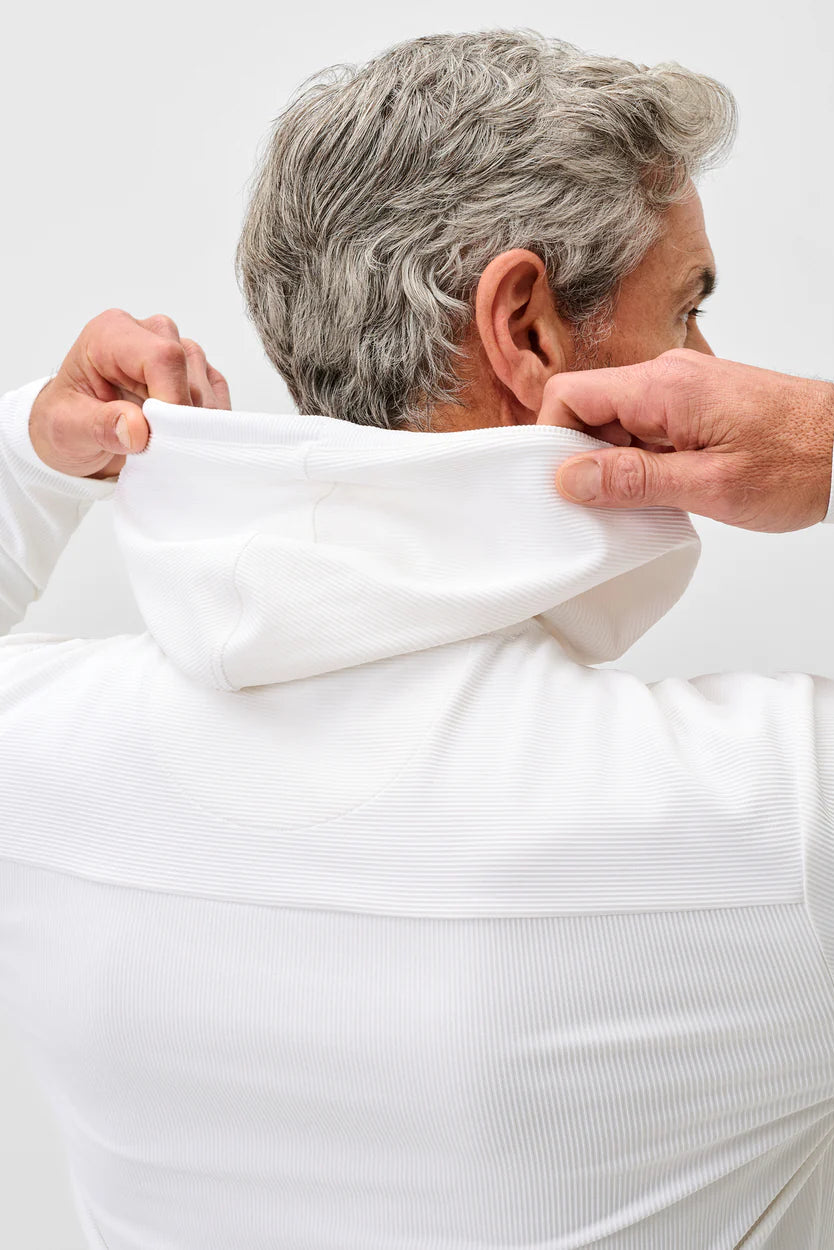 Person wearing a white long-sleeve shirt with a hood, adjusting it.