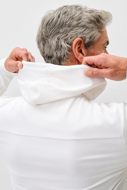 Person wearing a white long-sleeve shirt with a hood, adjusting it.