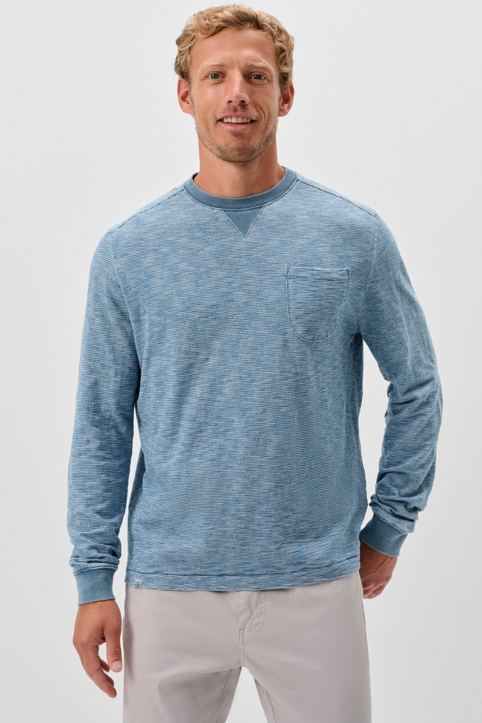 Man wearing a blue long-sleeve shirt with a pocket on a light gray background