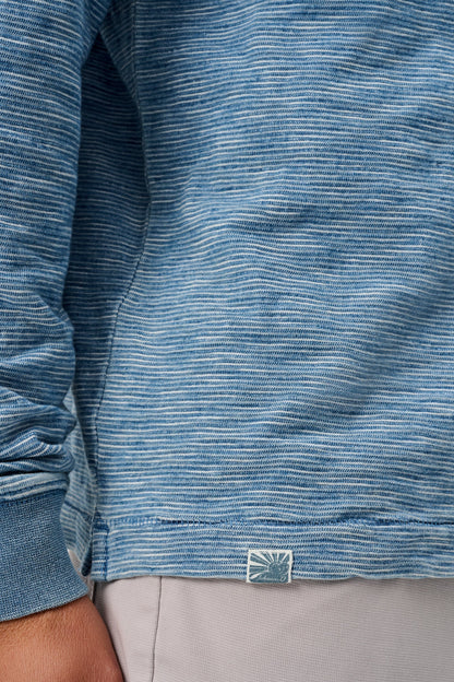 Close-up of a blue textured shirt with a brand logo on a person wearing gray pants.