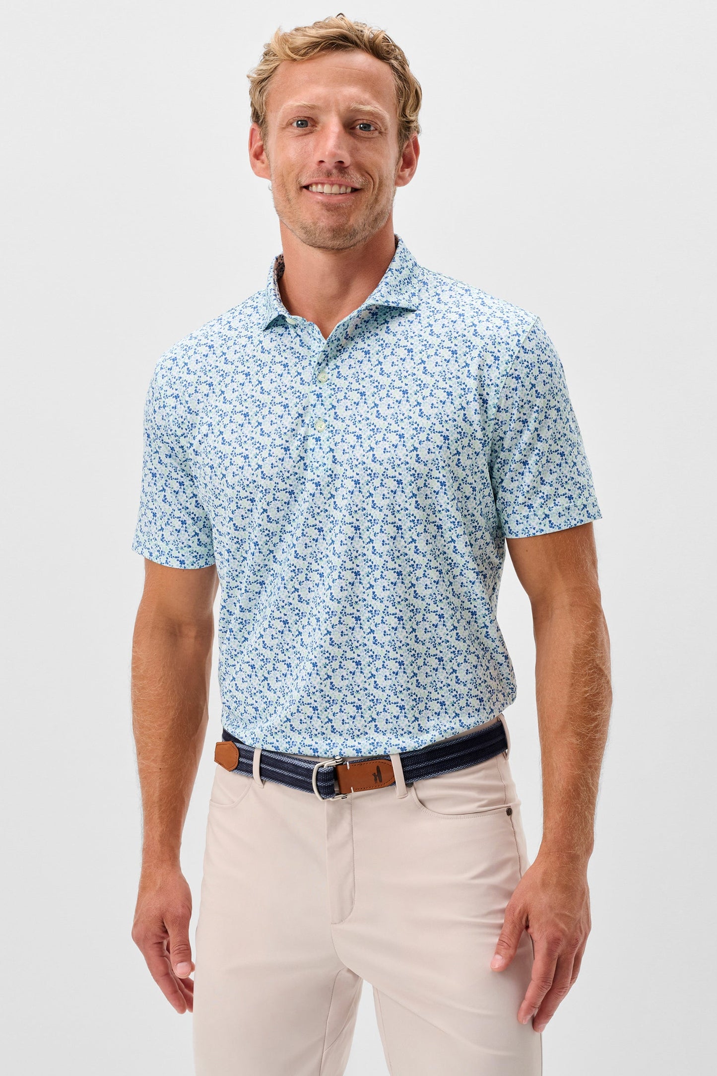 Man wearing a light blue patterned polo shirt and beige pants on a white background