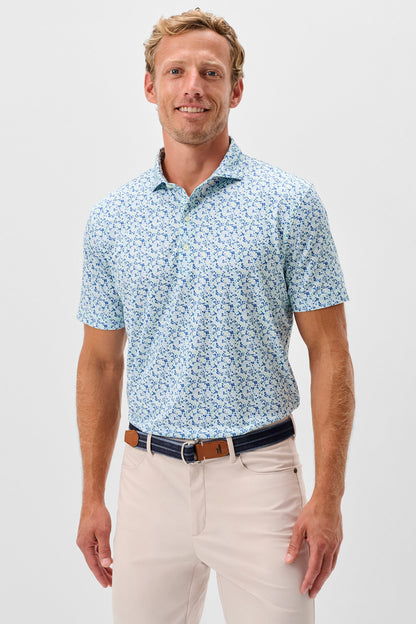 Man wearing a light blue patterned polo shirt and beige pants on a white background